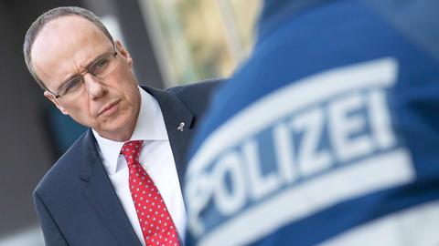 Innenminister Peter Beuth. So fotografiert, dass er auf den Rücken eines Polizeibeamten zu schauen scheint, auf dessen Rücken "Polizei" steht.