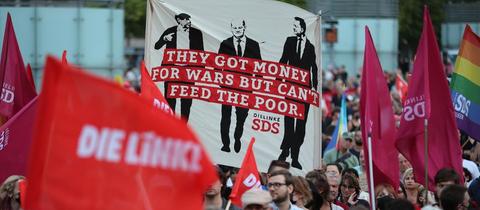 Protest gegen die Bundesregierung während einer Demo. Auf einem Banner steht z.B. "They got money for wars but can't feed the poor."