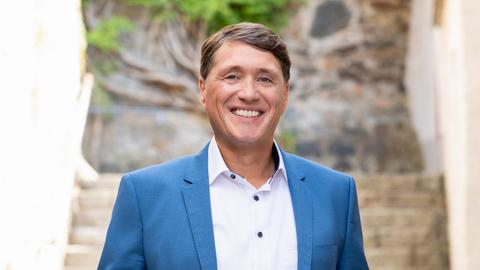 Lächelnder Mann, weißes Hemd, blaues Jackett, braunes Haar mit Seitenscheitel