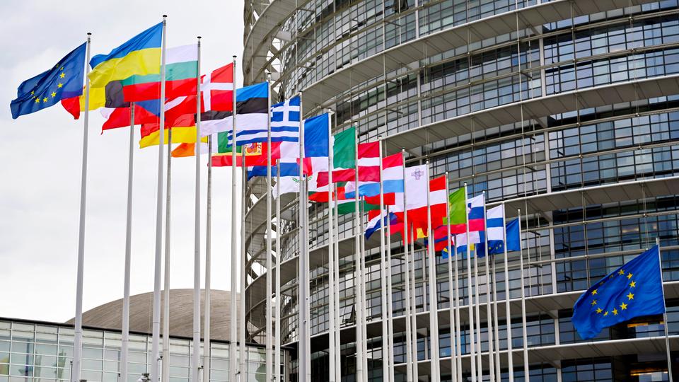 Ein runder, verglaster Bau mit den Flaggen der EU-Mitgliedsländer davor.