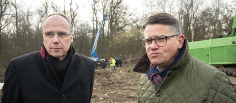 Peter Beuth und Boris Rhein stehen im Geände der Räumung und schauen in die Kamera.