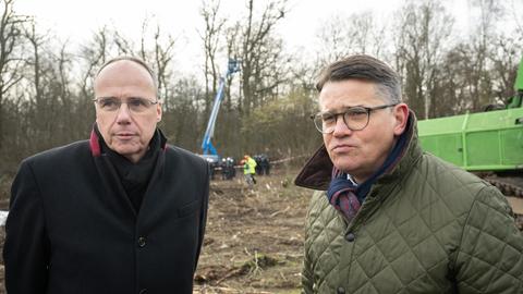 Peter Beuth und Boris Rhein stehen im Geände der Räumung und schauen in die Kamera.