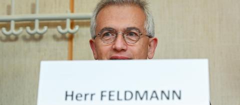 Peter Feldmann sitzt an einem Tisch - hinter einem Schild, auf dem "Peter Feldmann" steht. 