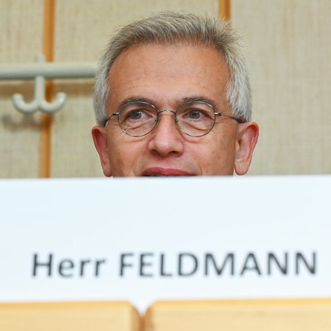 Peter Feldmann sitzt an einem Tisch - hinter einem Schild, auf dem "Peter Feldmann" steht. 