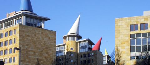 Ein Ensemble mehrgeschossiger Gebäude. Auf den Dächern der einzelnen Gebäude sind je ein farbiger Kegel zu sehen.