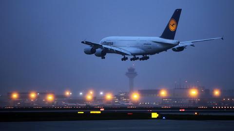 A380 der Lufthansa im Anflug auf die Landebahn im Dunkeln. Im Hintergund viele Lichter des Flughafens.