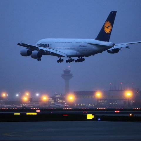 A380 der Lufthansa im Anflug auf die Landebahn im Dunkeln. Im Hintergund viele Lichter des Flughafens.