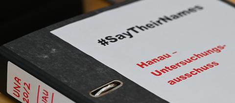 Großaufnahme eines Aktenordners auf welchem steht: "#say their names" und "Hanau-Untersuchungsausschuss".