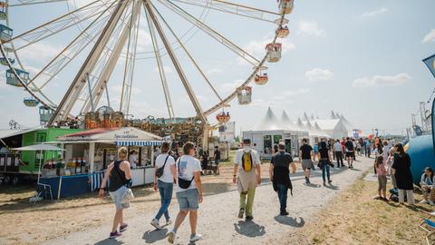 Das Bild zeigt Menschen, die über das Hessentagsgelände gehen. Im Hintergrund ist ein Riesenrad und Verkaufsstände zu sehen. 