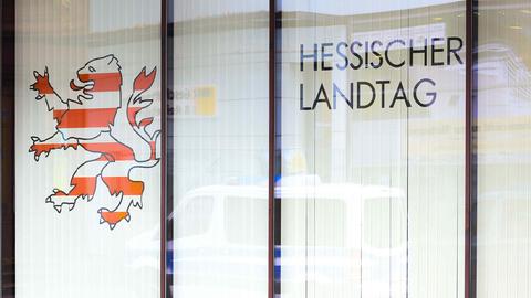 Foto einer Fensterscheibe auf welche "Hessischer Landtag" in großen Buchstaben und daneben ein "Hessenlöwe" geklebt sind. Hinter der Glasscheibe sind Jalousien.