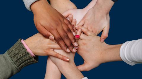 Hände von jungen Menschen verschiedener Hautfarbe liegen sternförmig übereinander.