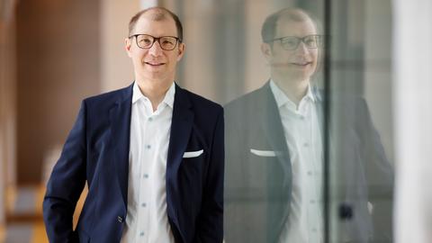 Jan Weckler: Mann im blauen Anzug und mit schwarzer Brille lehnt an Glastür.