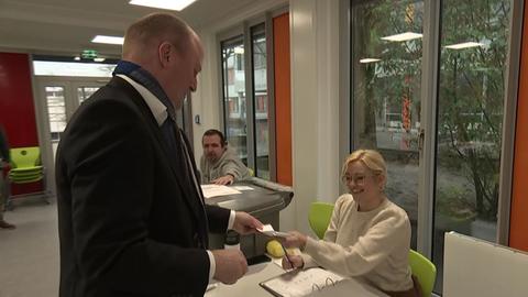 Becker gibt seinen gefalteten Stimmzettel einer Wahlhelferin