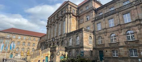 Das Rathaus in Kassel, zu sehen ist die große Treppe aus Stein, rechts und links zwei goldene Löwen. Im Vordergrund ist der Aschrottbrunnen zu sehen.