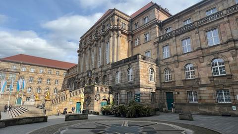 Das Rathaus in Kassel, zu sehen ist die große Treppe aus Stein, rechts und links zwei goldene Löwen. Im Vordergrund ist der Aschrottbrunnen zu sehen.