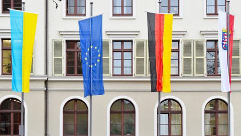 Vor einem Gebäude hängen vier Flaggen: die ukrainische in gelb-blau, die blaue Europaflagge, die schwarz-rot-goldene deutsche und die rot-weiße hessische Flagge.