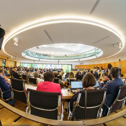 Fotot einer Plenarsitzung im hessischen Landtag. Im Vordergrund ein Kameramann an der Seite des Bildes.