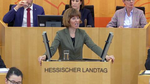 Eine Frau steht hinter einem Pult, auf dem "Hessischer Landtag" steht und spricht ins Mikrofon. Auf dem Bild ist ein Button zum Anklicken, damit ein Video abgespielt wird.