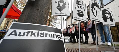 Menschen halten Schilder mit den Köpfen und Namen der Opfer von Hanau hoch. Im Vordergrund ein Schild mit dem Schriftzug "Aufklärung".