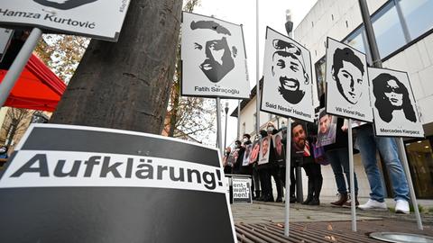 Menschen halten Schilder mit den Köpfen und Namen der Opfer von Hanau hoch. Im Vordergrund ein Schild mit dem Schriftzug "Aufklärung".