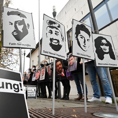 Menschen halten Schilder mit den Köpfen und Namen der Opfer von Hanau hoch. Im Vordergrund ein Schild mit dem Schriftzug "Aufklärung".