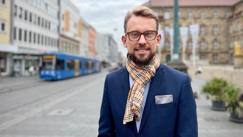 Maximilian Bathon (CDU) steht vor dem Kasseler Rathaus. Er trägt eine Brille und ein blaues Sakko mit Einstecktuch.
