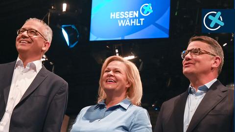 Tarek Al-Wazir, Nancy Faeser und Boris Rhein stehen nebeneinander auf einer Bühne und lachen.