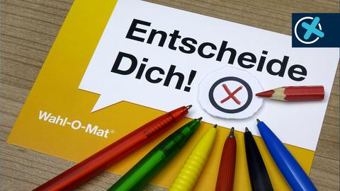 Zettel mit Aufschrift "Entscheide dich! Wahl-o-mat" und Stiften daneben in verschiedenen Farben, die Parteien zugeordnet werden können (blau, rot, grün, geld, usw.)