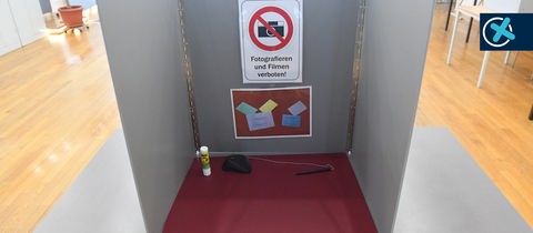 Ein Schild mit dem Schriftzug "Fotografieren und Filmen verboten!" hängt in einer Wahlkabine im.