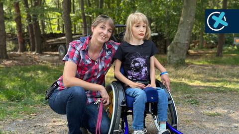 Silke Hable hat den Arm um ein im Rollstuhl sitzendes Mädchen gelegt. Beide lächeln.