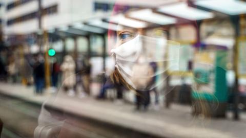 Eine Frau fährt mit Mundschutz U-Bahn. Ihr Gesicht spiegelt sich in der Fensterscheibe.