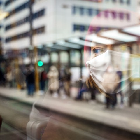 Eine Frau fährt mit Mundschutz U-Bahn. Ihr Gesicht spiegelt sich in der Fensterscheibe.