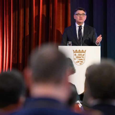 Boris Rhein (CDU), Hessischer Ministerpräsident, spricht bei einer Gedenkveranstaltung für die Opfer des Nationalsozialismus im Bürgerhaus der Stadt Bad Arolsen. Er steht hinter einem Pult mit dem Hessen-Wappen, vor ihm ein Mikrofon.