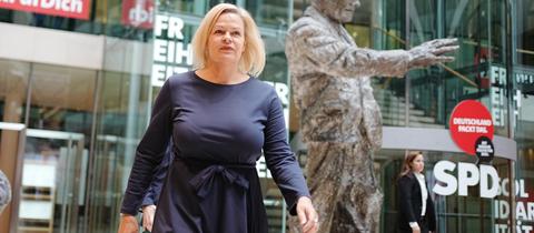 Eine Frau in einem blauen Kleid läuft an einer Bronzestatue vorbei.