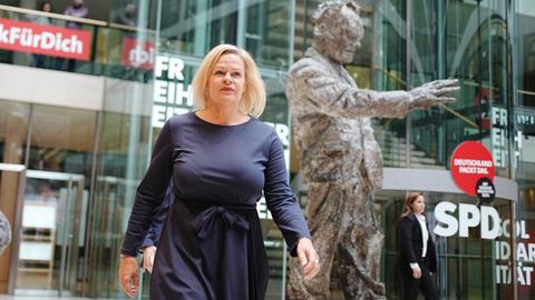 Eine Frau in einem blauen Kleid läuft an einer Bronzestatue vorbei.