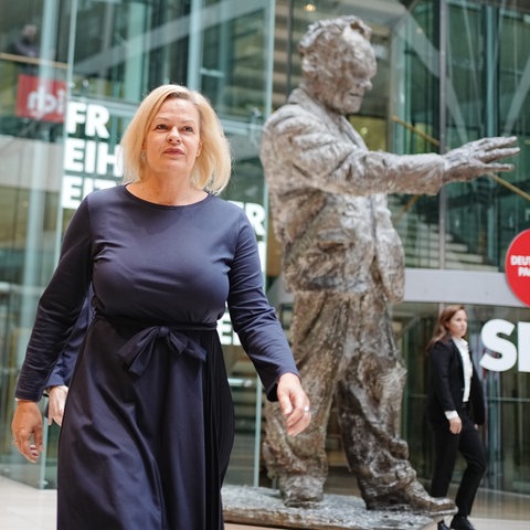 Eine Frau in einem blauen Kleid läuft an einer Bronzestatue vorbei.