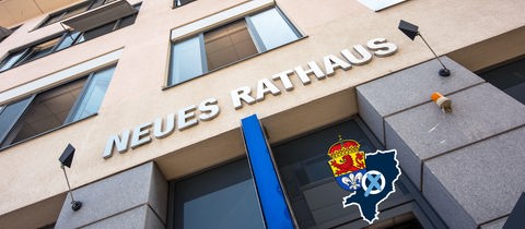 Foto von einem Gebäudeeingang, worüber "Neues Rathaus" steht - aus der Froschpersepektive fotografiert. Auf dem Bild eine kleine Grafik mit einer blau eingefärbten Fläche (Umriss der Stadt), dem Wappen der Stadt Darmstadt und einem Wahlkreuz.