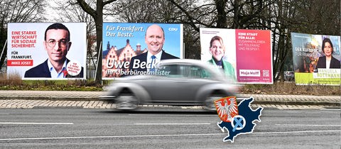 Wahlplakate am Rand einer Straße aufgereiht. Davor fährt ein Auto (unscharf). Auf dem Foto ein Label, bestehend aus dem Umriss und dem Wappen der Stadt Frankfurt und einem Wahlkreuz.