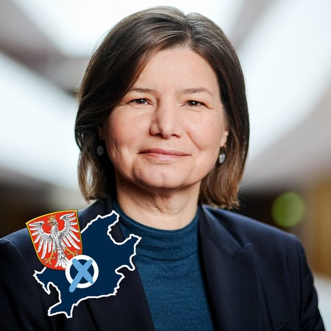 Portraitfoto Manuela Rottmann. Auf dem Bild ein kleines Label, das aus dem Umriß und dem Wappen der Stadt Frankfurt und einem Wahlkreuz besteht.