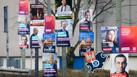 Viele Wahlplakate an Stangen im Straßenraum. Auf dem Foto ein Label, bestehend aus dem Umriss und dem Wappen der Stadt Frankfurt und einem Wahlkreuz.