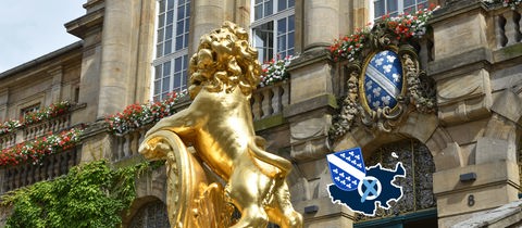 Bild eines historischen Gebäudes mit einem goldenen Löwen vor der Tür. Auf dem Foto eine kleine Grafik mit einer blau eingefärbten Fläche (Umriss Stadt Kassel), dem Wappen der Stadt und einem Wahlkreuz.