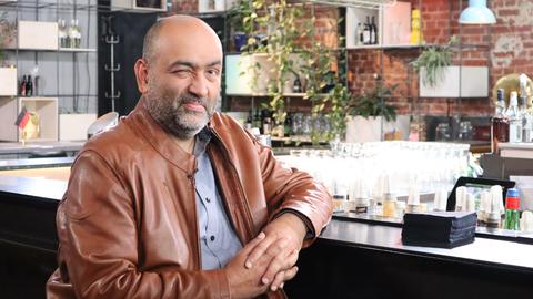 Omid Nouripour sitzt an einer Theke und zwinkert in die Kamera.