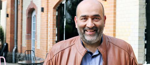 Omid Nouripour steht vor einer Bar in Gießen und lächelt in die Kamera.