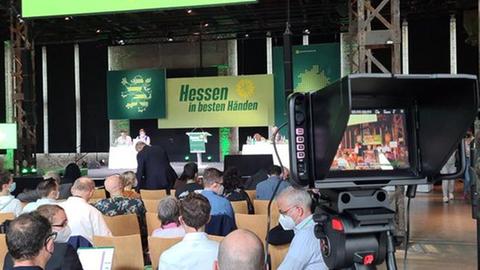 Menschen sitzen auf Stühlen vor einer Bühne, auf der ein Banner mit der Aufrischt "Hessen in besten Händen" hängt