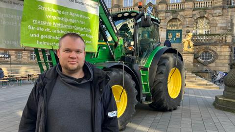 Maximilian Gundelach, einer der Organisatoren steht vor einem Traktor. Im Hintegrund ist das Kasseler Rathaus zu sehen.
