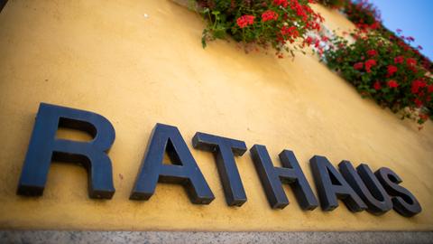 Schriftzug "Rathaus" an einer gelb gestrichenen Hauswand neben einer Blumenampel.