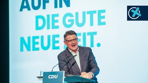 Ein Mann steht an einem Pult und spricht in ein Mikrofon. Am Pult steht "CDU". Im Hintergrund eine große türkisfarbene Wand auf welcher "Auf in die gute neue Zeit" in großen Lettern geschrieben steht.