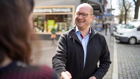 Rouven Kötter: Mann mit Brille gibt einer Frau die Hand und lacht