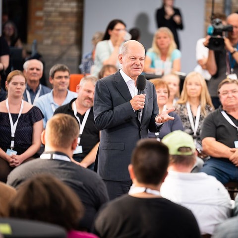 Bundeskanzler Olaf Scholz mit Mikrofon, umringt von Menschen