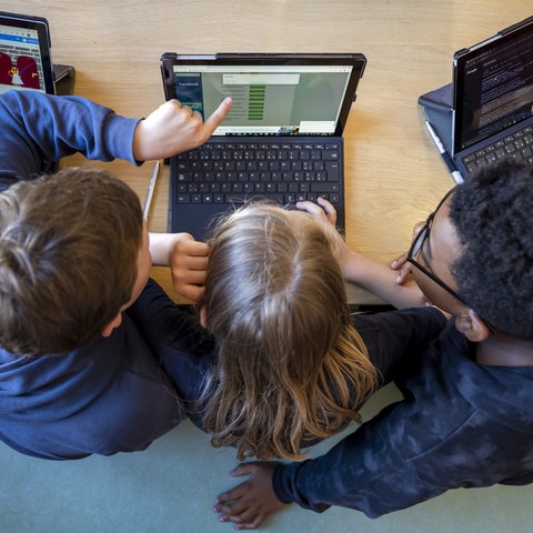 Drei Schüler zeigen auf Laptop